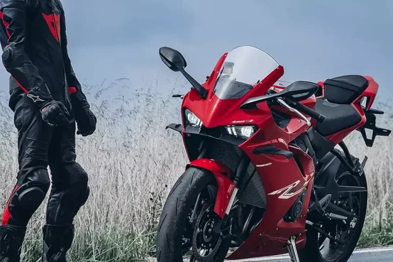 Red KOVE sportbike beside a standing rider in black and red leathers; “450 R” is legible on the front fairing