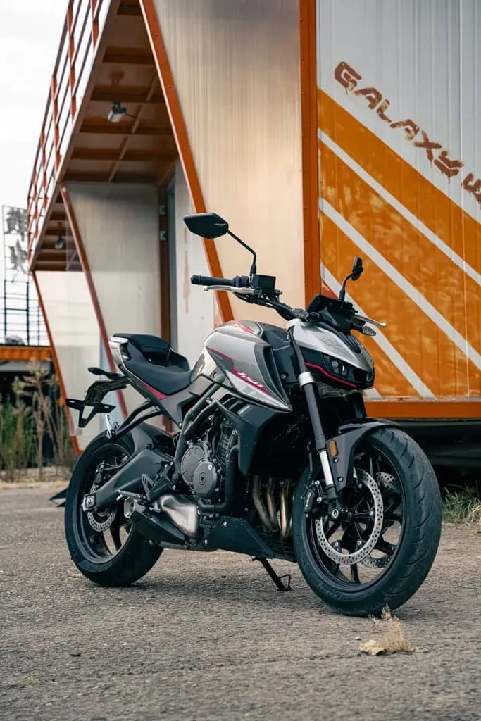 Silver-grey and black KOVE naked motorcycle parked on asphalt in front of a white and orange container