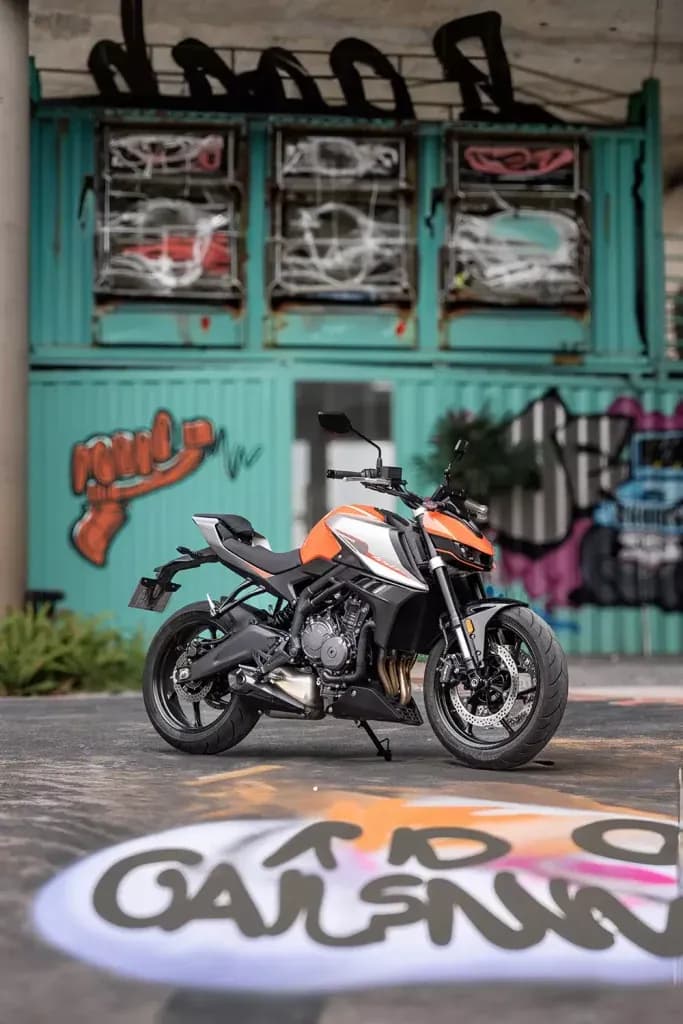 Orange, white and black KOVE naked motorcycle in front of turquoise graffiti-covered containers