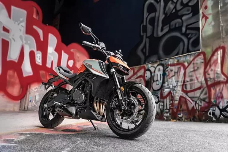 Orange and black KOVE naked motorcycle on grey pavement against walls covered in red and white graffiti