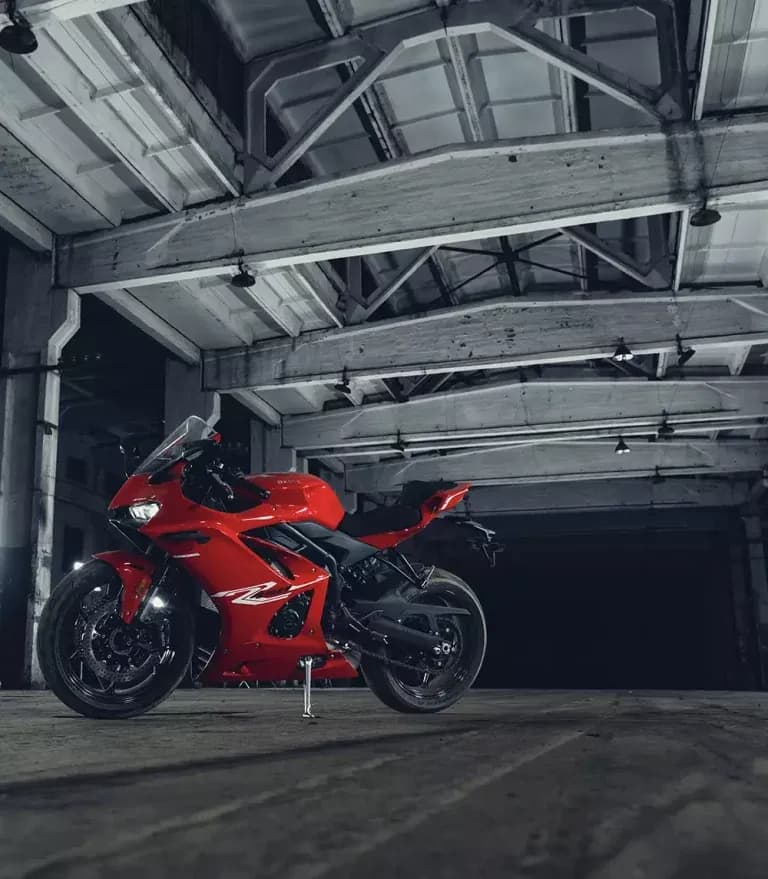 Red KOVE sportbike in side profile inside an abandoned industrial hall with concrete beams and overhead light