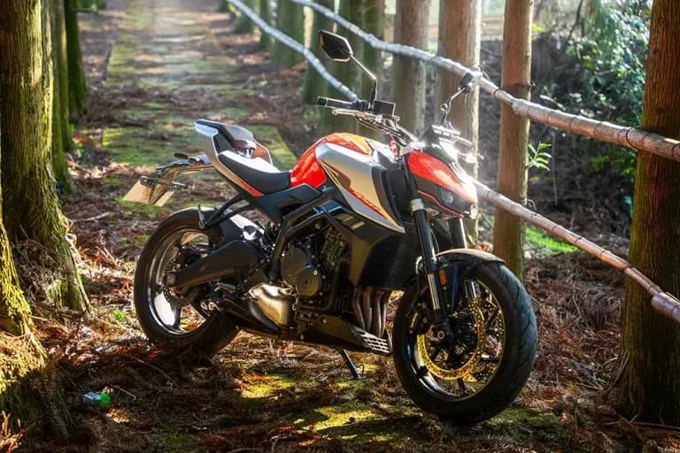 Silver, red and black KOVE naked motorcycle with gold wheels, parked on a path in a coniferous forest