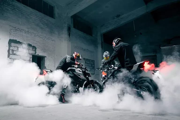 Two KOVE motorcycles and their riders performing burnouts inside a derelict building, engulfed in white smoke