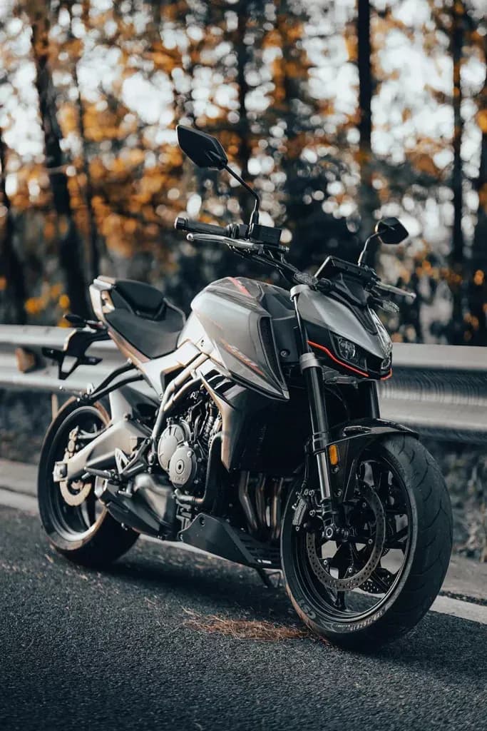 Grey and black KOVE naked motorcycle beside a road guardrail with blurred autumn foliage behind