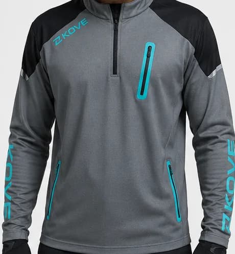 Heather grey long-sleeve technical jersey with a zip neck, black shoulder panels, a teal KOVE logo on the chest, a teal-zipped chest pocket, teal-zipped waist pockets and “KOVE” printed vertically down each sleeve; worn by a model in black gloves