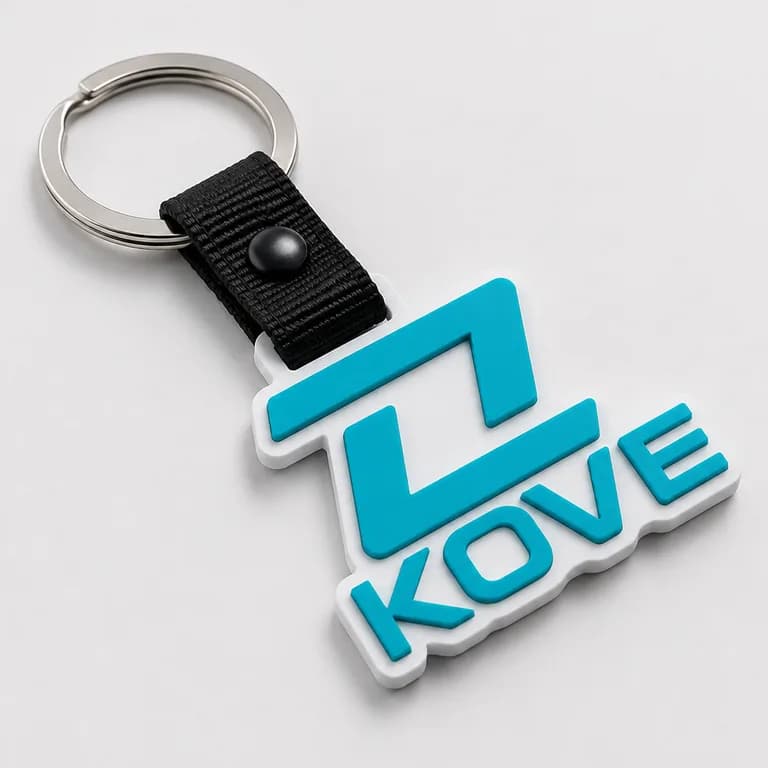 Rubber keyring moulded in the shape of the KOVE logo, teal on a white base, joined by a black snap strap to a metal split ring